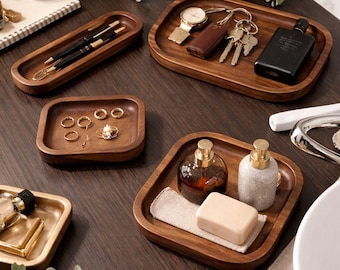 May include: A collection of five wooden trays in various shapes and sizes, including rectangular, square, and elongated designs. These trays are crafted from dark wood with a smooth finish, serving as organizers for pens, keys, jewelry, and toiletries.