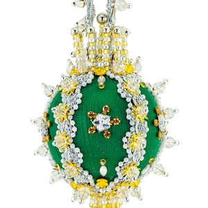 May include: A green Christmas ornament with intricate beadwork and embellishments. The round ornament features a central design with a star-shaped pattern, surrounded by silver, gold, and clear beads. It hangs from a silver cord.