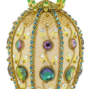 May include: An ornate, egg-shaped pendant with a gold chain. The pendant is cream-colored, adorned with iridescent gemstones, blue and clear crystals, and gold filigree. Green and gold accents complete the design.