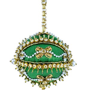 May include: A green, orb-shaped ornament with gold and pearl embellishments. The ornament features a gold hanging chain and a crystal pendant. The surface is decorated with gold floral designs and white pearls, creating a festive and elegant appearance.