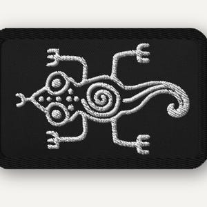 May include: A rectangular black embroidered patch featuring a white stitched lizard design. The lizard has a spiral pattern on its body, circular eyes, and a forked tongue. The patch has a thick black stitched border and rounded corners.
