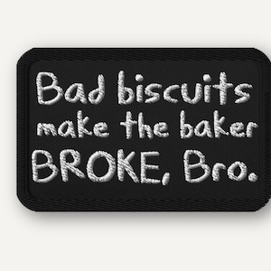 May include: Black rectangular patch with white embroidered text that reads "Bad biscuits make the baker BROKE, Bro." The patch has a black border and is likely an iron-on or sew-on patch.