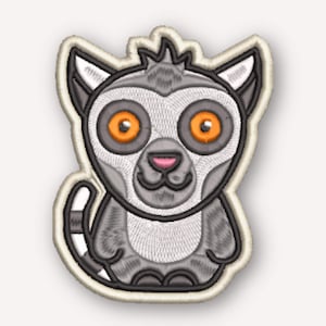 May include: An embroidered patch featuring a stylised lemur with large, bright orange eyes, a grey and white face, and a grey body with dark grey stripes. The lemur has a small pink nose, pointed ears, and a long, striped tail, all outlined in black.