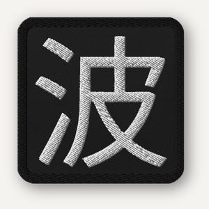 May include: Square black embroidered patch featuring a white Japanese Kanji character. The character is stylized with thick, textured lines. The patch has a black border and is likely designed to be sewn or ironed onto fabric.