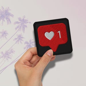 Flat lay of Micro Influencer patch iron-on with red Instagram heart icon, 1 Like text, on neutral background, showing crisp embroidery and playful self-deprecating humor, perfect for jackets, backpacks, or gifts.
