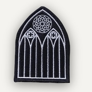 Puede incluir: Parche bordado en blanco y negro con forma de ventana de catedral gótica. El diseño incluye una vidriera circular y líneas verticales. Este parche probablemente está destinado a la ropa o accesorios, añadiendo una estética gótica.
