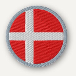 May include: A circular embroidered patch featuring the flag of Denmark with a red background and a white Nordic cross. The patch has a light gray stitched border around the entire circumference, showcasing detailed thread texture throughout.