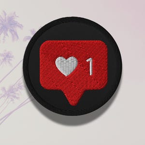Flat lay of Micro Influencer patch iron-on with red Instagram heart icon, 1 Like text, on neutral background, showing crisp embroidery and playful self-deprecating humor, perfect for jackets, backpacks, or gifts.