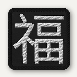 以下が含まれることがあります： 黒い正方形の背景に白い日本語の文字が刺繍されたパッチ。文字は様式化されており、記号のようです。パッチには黒い縁があり、布に縫い付けたり、アイロンをかけたりするように設計されています。