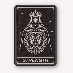 Puede incluir: Un parche rectangular negro bordado con un diseño de líneas blancas de una cabeza de león bajo una corona y un velo, sobre un fondo estrellado. La palabra STRENGTH está impresa en letras mayúsculas blancas dentro de un borde inferior.