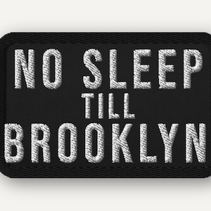 May include: Black rectangular patch with the embroidered text "NO SLEEP TILL BROOKLYN" in white. The patch has a black border and a textured appearance, suggesting it's made of fabric.
