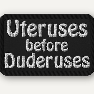 Può includere: Una toppa rettangolare nera ricamata con angoli arrotondati che presenta il testo bianco ricamato Uteruses before Duderuses. Il design è centrato su uno sfondo nero solido con un bordo nero spesso che circonda l'intera toppa.