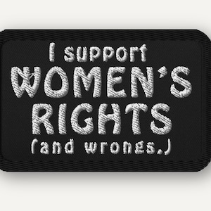 Puede incluir: Un parche rectangular negro bordado con un borde cosido. El texto blanco dice: I support WOMEN'S RIGHTS (and wrongs.) Las letras están en un estilo de fuente sans-serif en negrita, creando un diseño de alto contraste sobre el fondo de tela oscura.