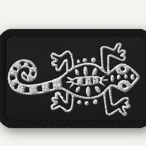 May include: Black rectangular patch with a white embroidered lizard design. The lizard is stylized with a patterned body, curled tail, and dotted accents. The patch has a black border.