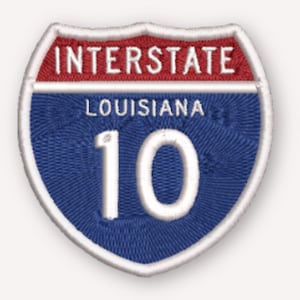 May include: An embroidered patch shaped like a shield, featuring a red top section with the white text INTERSTATE, a blue bottom section with the white text LOUISIANA and the number 10, all outlined with a thick white border.
