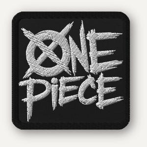 Op de afbeelding: Geborduurde patch met de woorden "ONE PIECE" in witte, gestileerde letters. De tekst staat op een zwarte, vierkante patch met afgeronde hoeken. Het ontwerp bevat een doorgestreepte cirkel boven het woord "ONE".