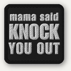 May include: Black square patch with white embroidered text that reads "mama said KNOCK YOU OUT". The patch has a black border and a textured appearance, suitable for sewing onto clothing or accessories.
