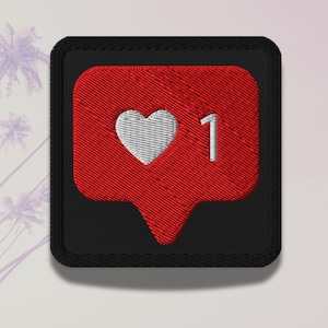 以下が含まれることがあります： 赤い吹き出しに白いハートと数字の1が刺繍されたパッチ。パッチは黒い縁取りがあり、布にアイロンをかけたり縫い付けたりするように設計されています。デザインはソーシャルメディアの「いいね」アイコンを連想させます。