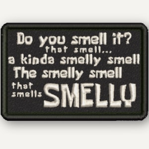 Puede incluir: Un parche rectangular negro bordado con un borde blanco. El texto dice: Do you smell it? that smell... a kinda smelly smell The smelly smell that smells SMELLY. Las letras son blancas y presentan un estilo de fuente tipo bloque.