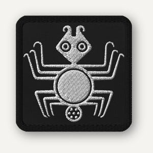 May include: A square black embroidered patch featuring a white stitched graphic of a stylized spider with a diamond-shaped head, two circular eyes, six legs, and a small circular body segment at the bottom containing six small white dots.