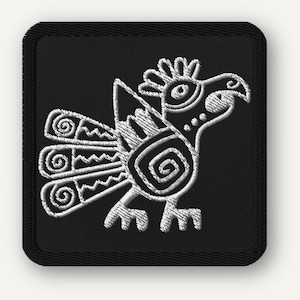 May include: Embroidered patch featuring a stylized white bird design on a black square. The bird has a detailed, symmetrical pattern with spiral and zigzag elements. The patch has a black border.