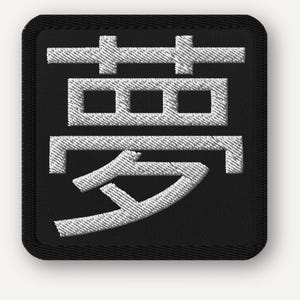 Puede incluir: Un parche cuadrado negro bordado con el carácter japonés Kanji para "sueño" en blanco. El carácter está colocado en el centro y cosido con un efecto texturizado, sobre un fondo negro liso.