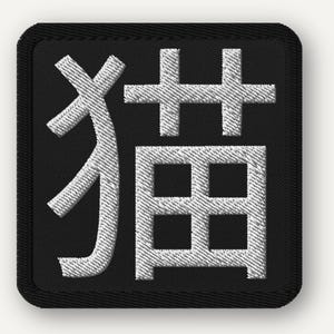 May include: Embroidered patch featuring a Japanese Kanji character, 猫, meaning "cat." The design is a white, textured stitch on a black square background with a black border. This patch is suitable for clothing or accessories.