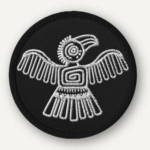 May include: A circular embroidered patch featuring a black background with a white stitched graphic of a stylized bird with outstretched wings. The bird design includes geometric spiral patterns on the chest and head with a detailed tail.