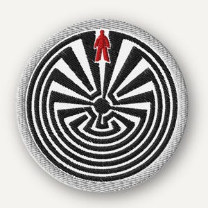 May include: Circular embroidered patch with a black and white maze design and a red figure. The patch has a grey border. Ideal for customising clothing or bags, the design is intricate and eye-catching.
