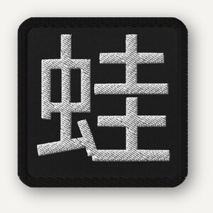 May include: Embroidered patch with a white Japanese Kanji character on a black square. The character is a stylized symbol. The patch has rounded corners. The design is simple and bold.