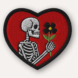 May include: Embroidered patch in the shape of a heart with a red background and a black border. The patch features a white skeleton holding a black flower with green leaves. The skeleton is in profile.