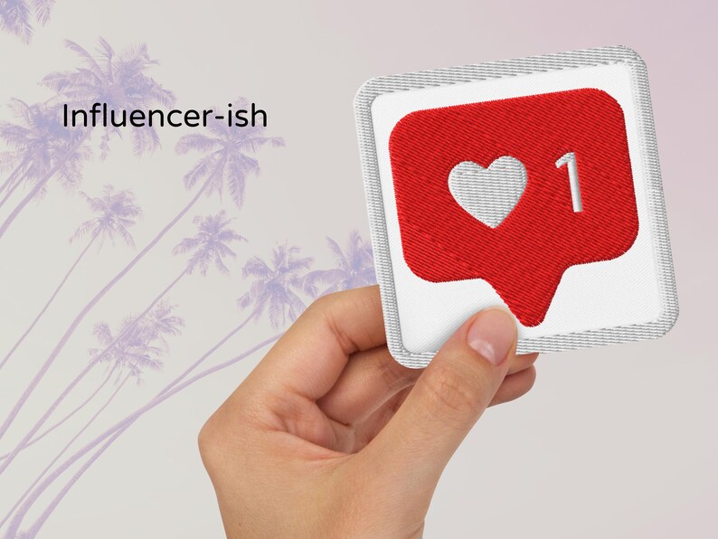 Flat lay of Micro Influencer patch iron-on with red Instagram heart icon, 1 Like text, on neutral background, showing crisp embroidery and playful self-deprecating humor, perfect for jackets, backpacks, or gifts.