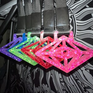 May include: Five colorful, glittery, diamond-shaped keychains with black lanyards. The keychains are in shades of purple, green, red, and pink.