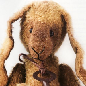 Puede incluir: Un conejo de peluche de estilo vintage, de color marrón, con largas orejas caídas y un colgante de llave. El conejo tiene un aspecto envejecido y texturizado. La llave es de color marrón óxido.