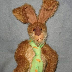 Può includere: Un coniglio di peluche marrone che indossa una cravatta verde e arancione con un motivo a carota. Il coniglio ha la pelliccia marrone e un naso lungo.