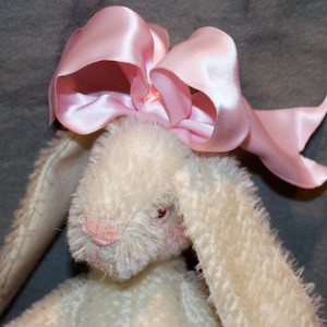 May include: A white plush bunny with long ears and a pink satin bow on its head.
