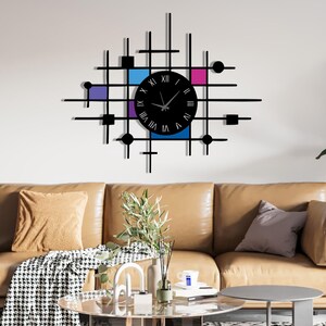 May include: Black wall clock with a modern geometric design. The clock face is black with Roman numerals. The design includes a grid pattern with squares, circles, and rectangles in black, with blue, purple, and pink accents.