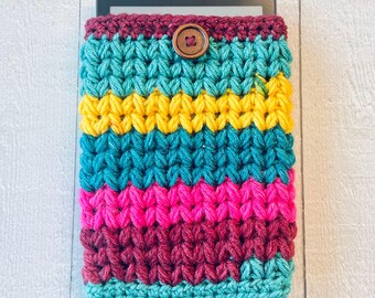 May include: A colorful crocheted e-reader cover with a brown button. The cover has stripes of teal, yellow, pink, and maroon.