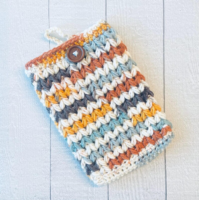 May include: A crocheted phone case with a chevron pattern in shades of blue, orange, yellow, and brown. The case has a brown button closure.
