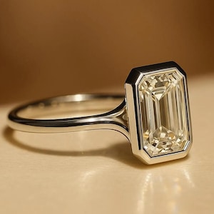 May include: A silver ring with a large, rectangular, light-yellow gemstone. The gemstone is set in a bezel setting, and the band is thin and polished. The ring is displayed on a light-colored surface.