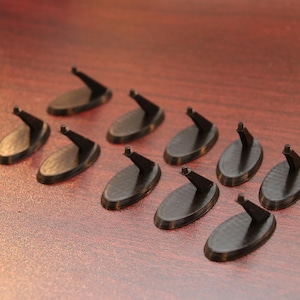 May include: Nine black plastic display stands for figurines or other small objects. The stands are oval shaped with a raised hook on one end.