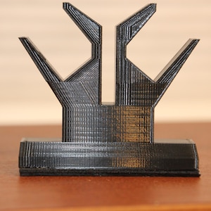 May include: A black 3D printed stand with two prongs on top, designed to hold a pair of headphones.