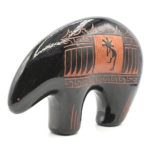 May include: A black ceramic bear figurine with a glossy finish. The bear features etched designs in a reddish-brown colour, including a Kokopelli figure and geometric patterns. The figurine has a rounded body and a stylised appearance.