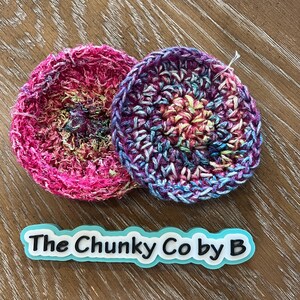 May include: Two circular crochet items in bright colours. One is mainly pink, the other a mix of blues, purples, and yellow. The text "The Chunky Co by B" is displayed on a light blue and white label.