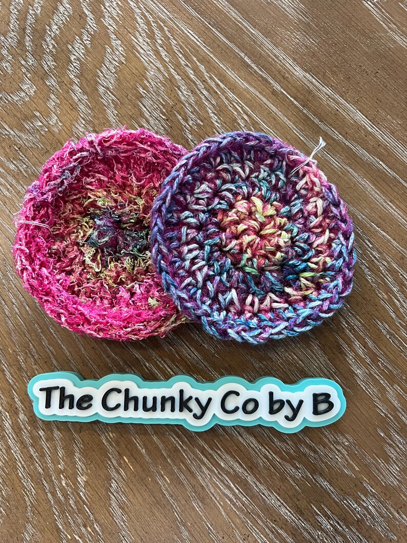 May include: Two circular crochet items in bright colours. One is mainly pink, the other a mix of blues, purples, and yellow. The text "The Chunky Co by B" is displayed on a light blue and white label.