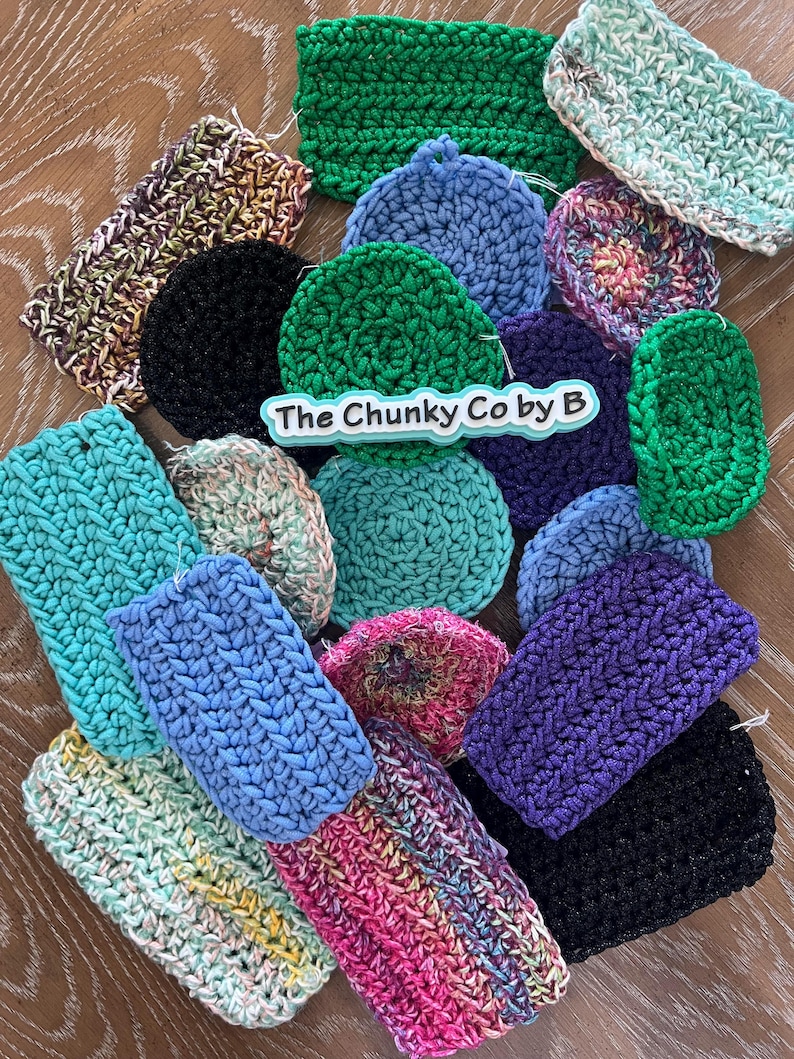 May include: A selection of handmade crochet items in various shapes and colours, including green, blue, purple, and multi-coloured pieces. The items are arranged on a wooden surface, with the text "The Chunky Co by B" visible.
