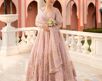 Puede incluir: Una mujer con un vestido rosa bordado con una chalina a juego, sosteniendo un ramo de flores blancas. Está de pie en un balcón con un suelo de baldosas rosa y blancas.