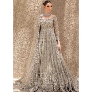 Puede incluir: Un vestido largo y fluido de color gris plateado con intrincados abalorios y bordados. El vestido presenta mangas largas, un cuello alto y una falda amplia. Un chal a juego y un collar de cuentas completan el elegante conjunto, perfecto para eventos formales.