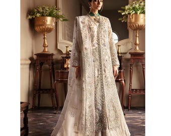 May include: An ivory-colored, long-sleeved gown with intricate embroidery and embellishments. The gown features a flowing skirt and a matching shawl. The design includes silver and pink accents, creating an elegant and detailed look. The outfit is suitable for formal events.