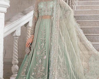 Puede incluir: Un vestido largo de color verde claro con intrincados bordados plateados y una superposición transparente. El vestido tiene un corpiño ajustado y una falda fluida con un dobladillo con volantes. La modelo lleva un dupatta a juego con un borde plateado.